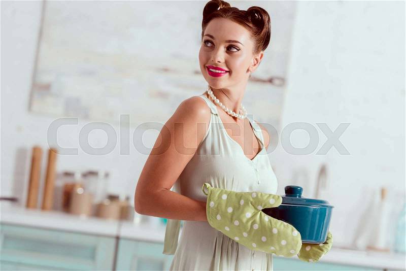 Smiling pin up girl standing in kitchen and holding pot , stock photo
