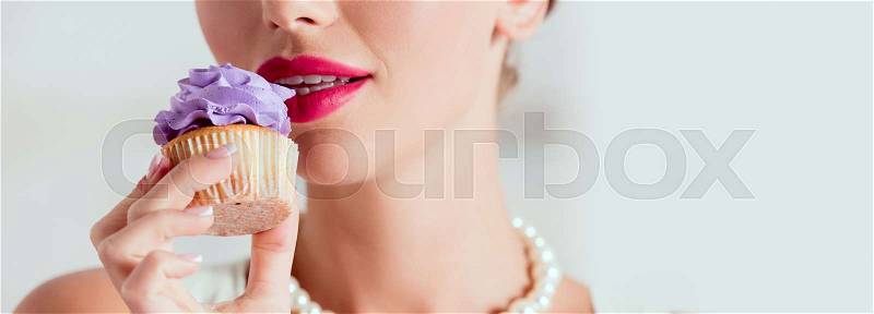 Partial view of pin up girl tasting homemade cupcake with purple cream , stock photo