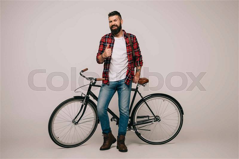 Handsome smiling man in checkered shirt posing with bicycle and showing thumb up on grey, stock photo