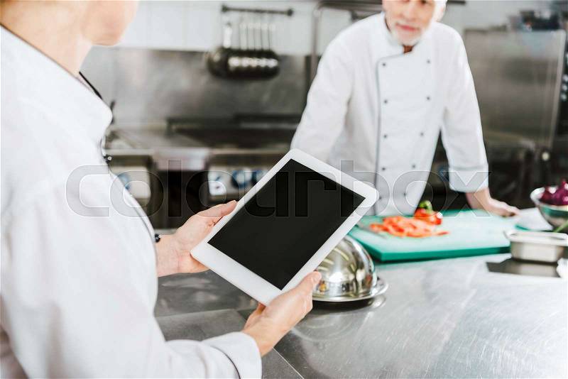 Partial view of female chef using digital tablet with blank screen in restaurant kitchen, stock photo