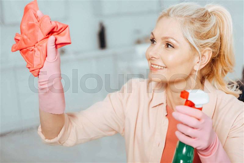 Glad senior woman with pony tail cleaning window with spray and rag, stock photo