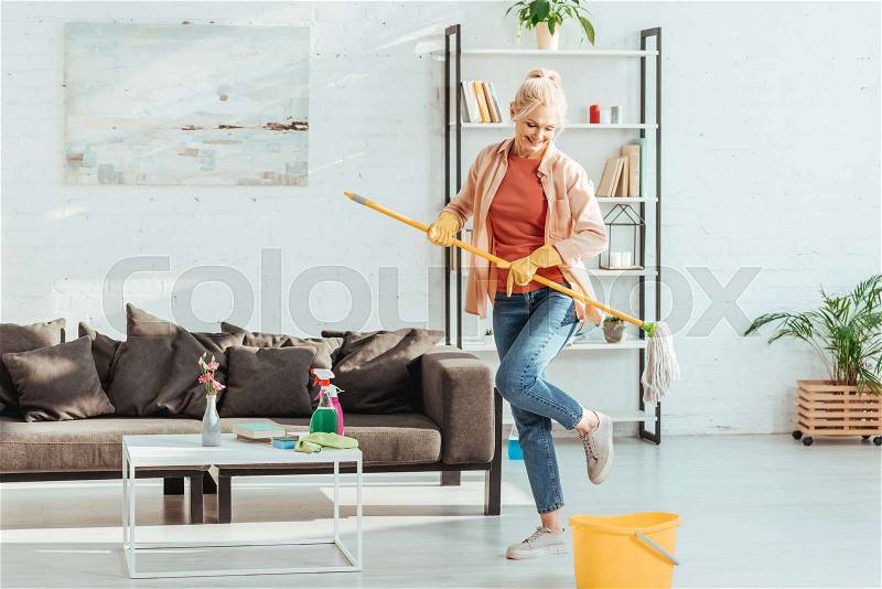 Gorgeous senior woman dancing while cleaning floor in living room, stock photo