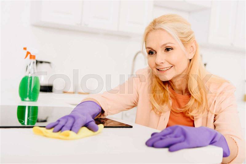 Smiling senior woman in rubber gloves cleaning stove, stock photo