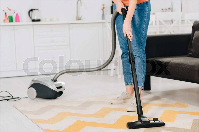 Cropped view of woman in jeans cleaning carpet with vacuum cleaner, stock photo