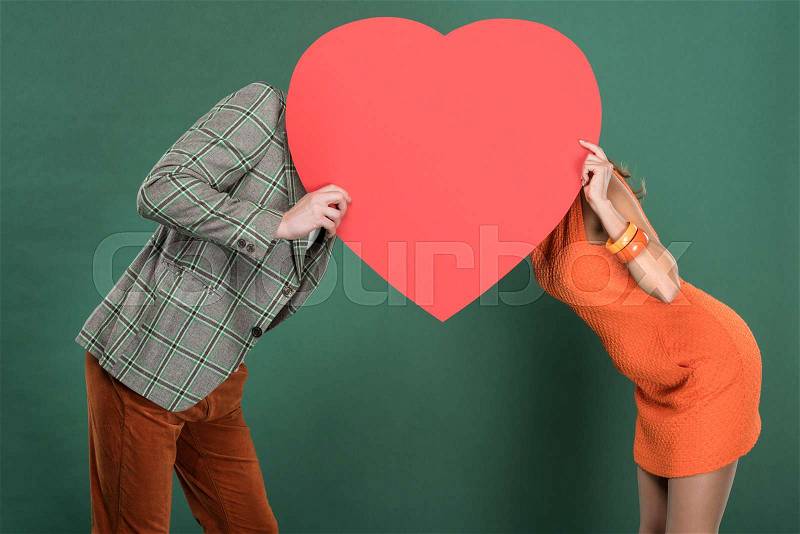 Man and woman covering faces with heart shaped paper card isolated on green, stock photo