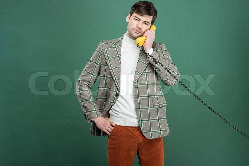Handsome man in vintage clothes talking on retro telephone isolated on green, stock photo