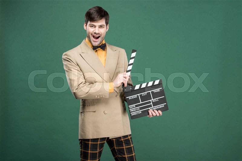Excited handsome man in vintage clothes looking at camera and holding film clapperboard isolated on green, stock photo