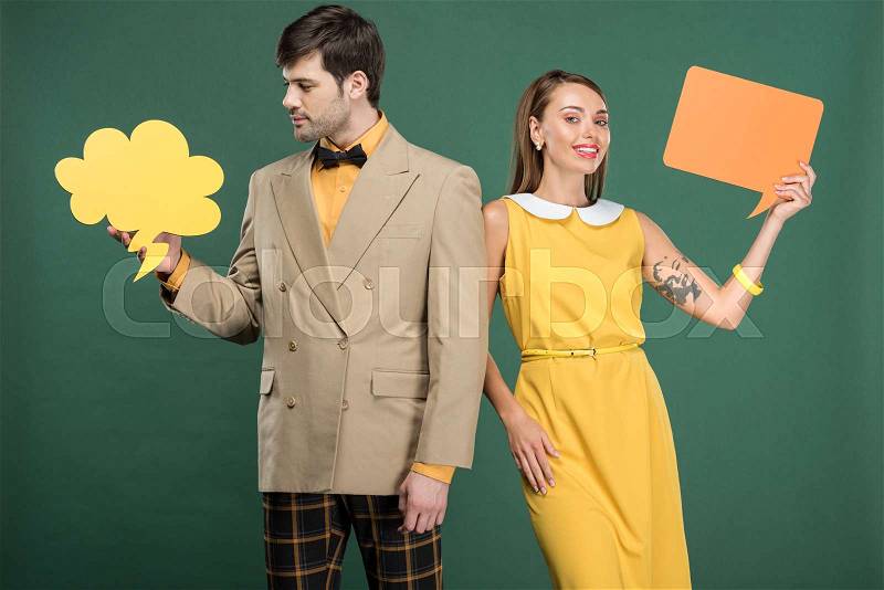 Attractive couple in vintage clothes holding speech bubble and thought bubble isolated on green, stock photo