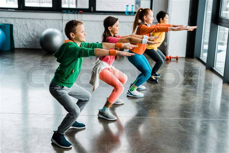 Group of kids doing squats in gym, stock photo