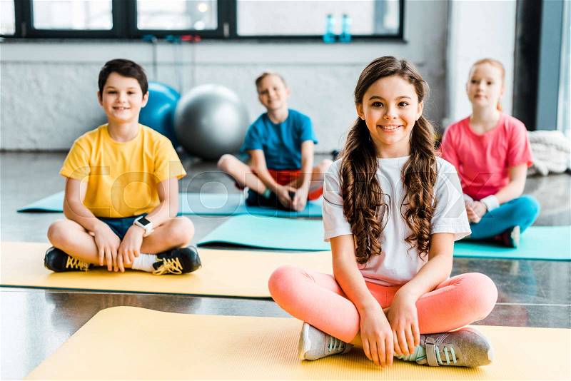 Excited kids stretching on fitness mats in gym, stock photo