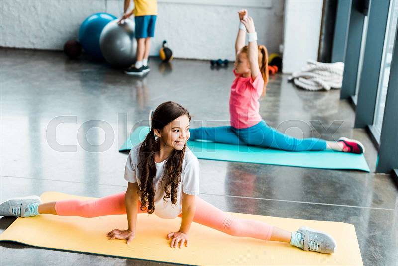 Cute kids doing twine on fitness mats in gym, stock photo