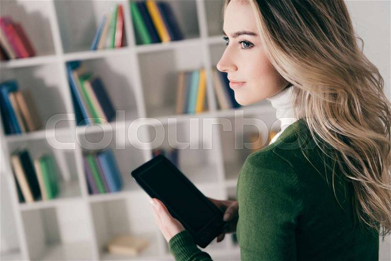 Beautiful woman holding e-book near bookshelf at home , stock photo