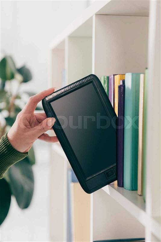 Cropped view of woman taking ebook with blank screen from bookshelf, stock photo