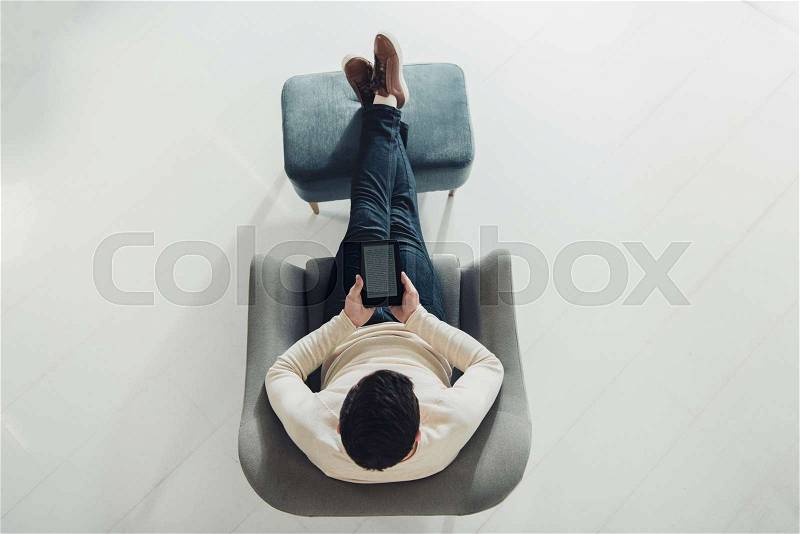 Top view of man reading e-book while sitting in armchair at home, stock photo