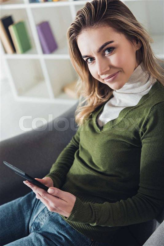 Cheerful woman holding e-reader and smiling at home , stock photo