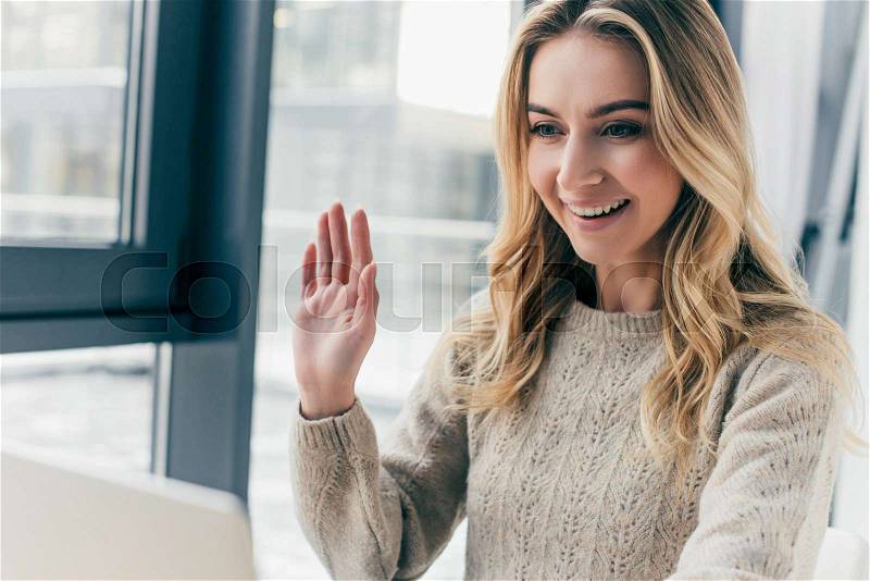 Cheerful woman waving hand while having video call , stock photo