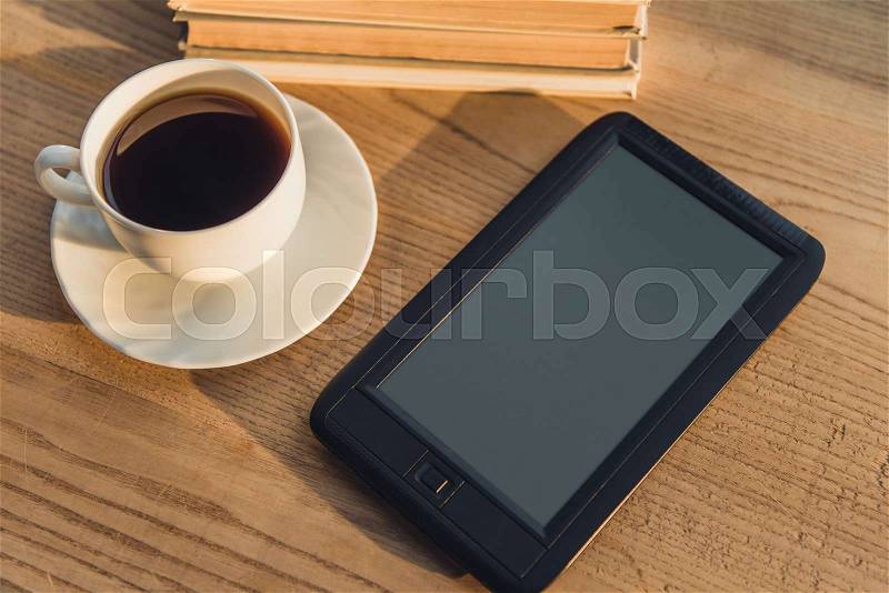 Black e-reader with blank screen lying near cup with coffee on table , stock photo