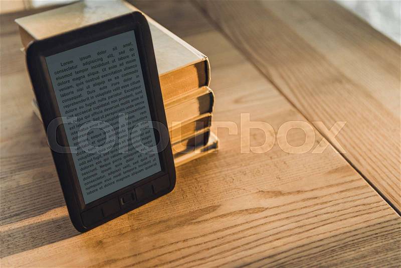 Black ebook near paper books on wooden table, stock photo