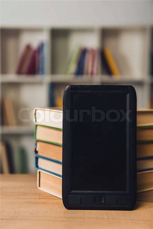 Ebook with blank screen near paper books on table, stock photo