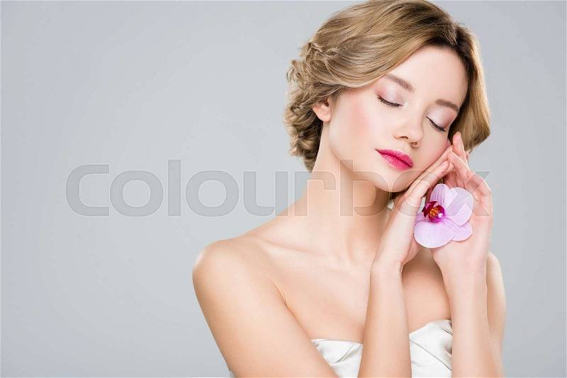 Young tender woman with closed eyes holding purple orchid isolated on grey, stock photo