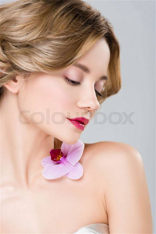 Young tender woman with purple orchid on shoulder isolated on grey, stock photo