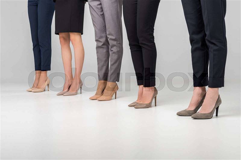Cropped view of women standing in hight heel shoes on grey background, stock photo