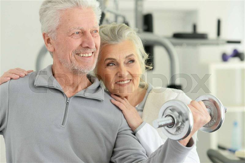 Active smiling senior couple exercising posing in gym, stock photo