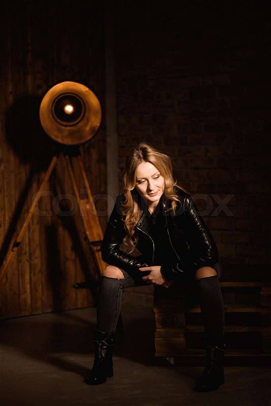 Sexy blonde woman in leather clothes posing against wooden studio wall, stock photo