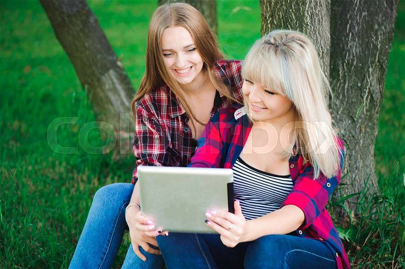 Holidays, technology and tourism concept - two beautiful girls looking into tablet pc, stock photo