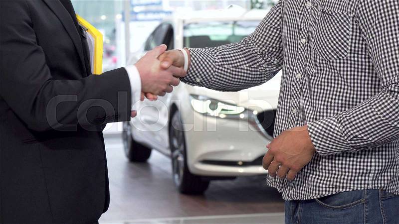 Car dealer shaking hands with client and passing car keys to the man. Cropped shot of a man buying new car, receiving car key and shaking hands with salesman. ..., stock photo