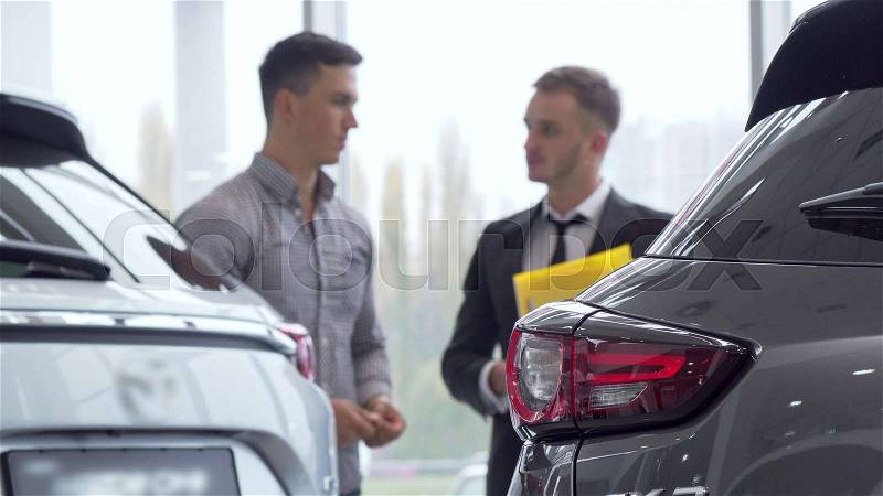 Selective focus on a car, male customer talking to auto dealer on the background. Man buying new automobile, getting an advice from salesman. Ownership, insurance ..., stock photo