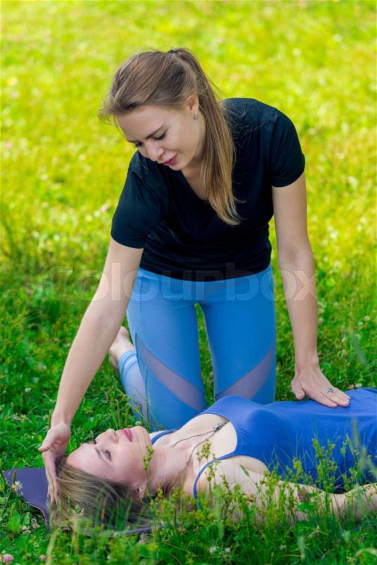 Coach girl controls woman\'s breathing exercises during yoga, shooting in summer park, stock photo