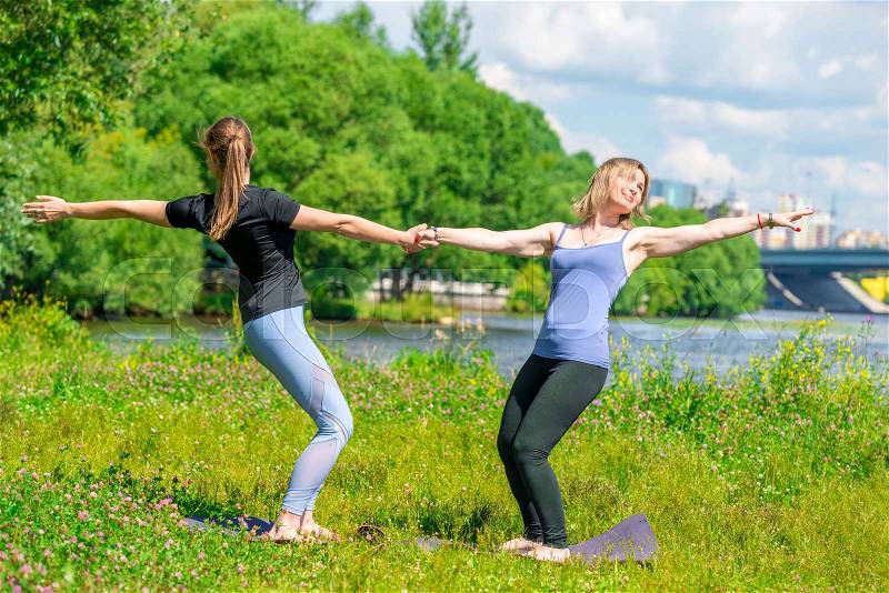 Women in a pair doing yoga exercises in the park on the grass , stock photo