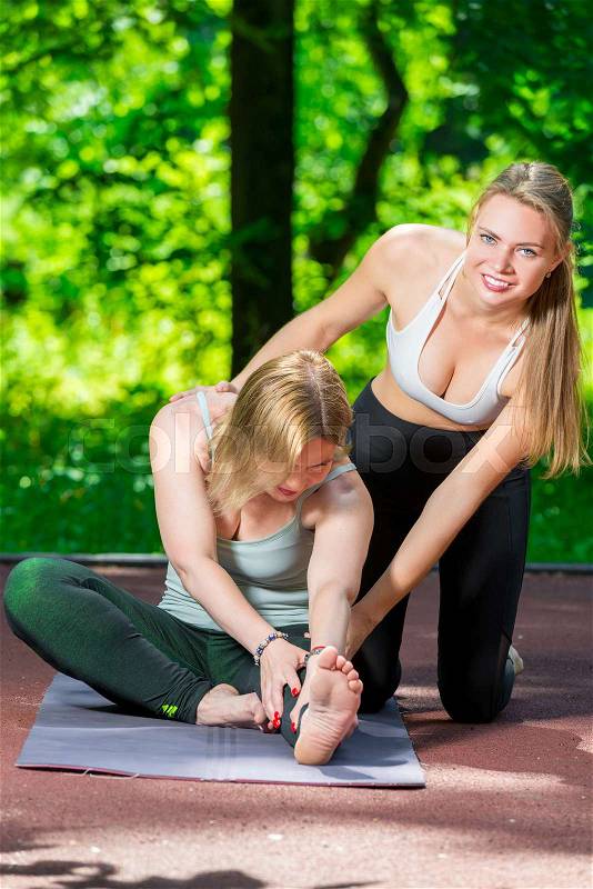 In the park, a yoga trainer helps a woman to do stretching exercises, stock photo