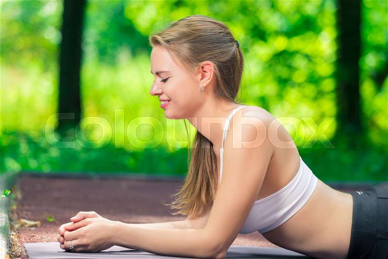 Smiling slim woman playing sports in a summer park, portrait while doing an exercise, stock photo