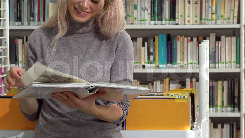 Female reader turning over pages of a book while reading at library. Cropped shot of a cheerful woman smiling, reading a book. Female student studying at college. ..., stock photo