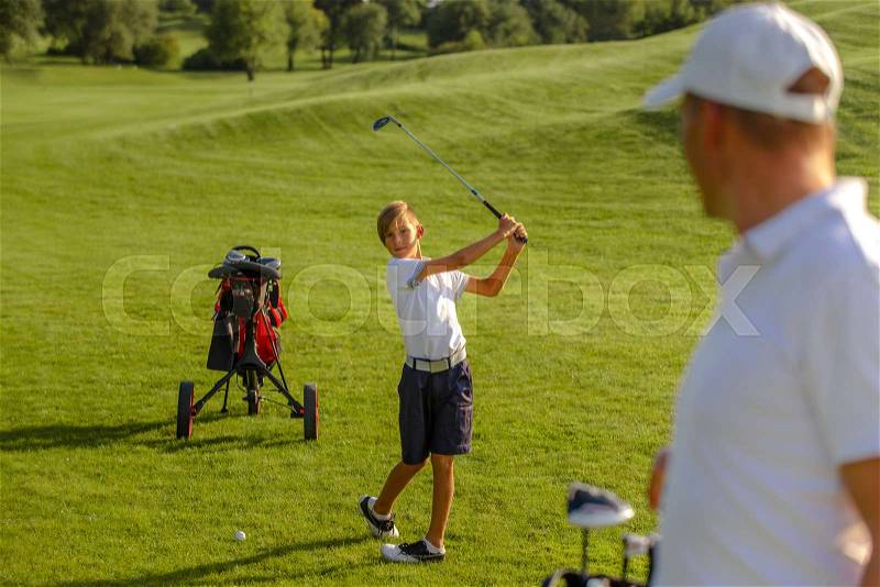 11 years old boy playing golf with his father or trainer at golf course on warm autumn day, stock photo