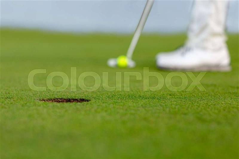 Image of golf hole on green. Golfer is ready to putt a yellow ball into hole, stock photo