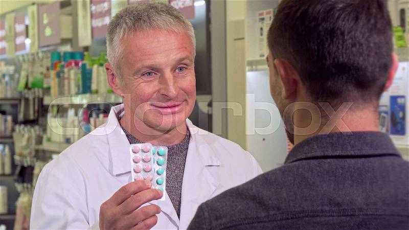Senior pharmacist giving blisters with pills to a male customer. Experienced chemist selling medication to the client, working at drugstore. Sales, health care, ..., stock photo