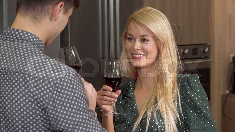Gorgeous happy woman drinking wine at home with her boyfriend. Beautiful woman sipping red wine, celebrating with her husband in the kitchen. Valentines day, love ..., stock photo