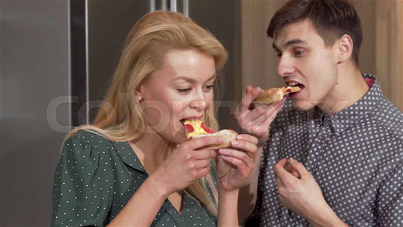 Happy couple enjoying delicious pizza in their new apartment in the kitchen. Beautiful woman and her handsome boyfriend enjoying Valentines day at home, eating ..., stock photo
