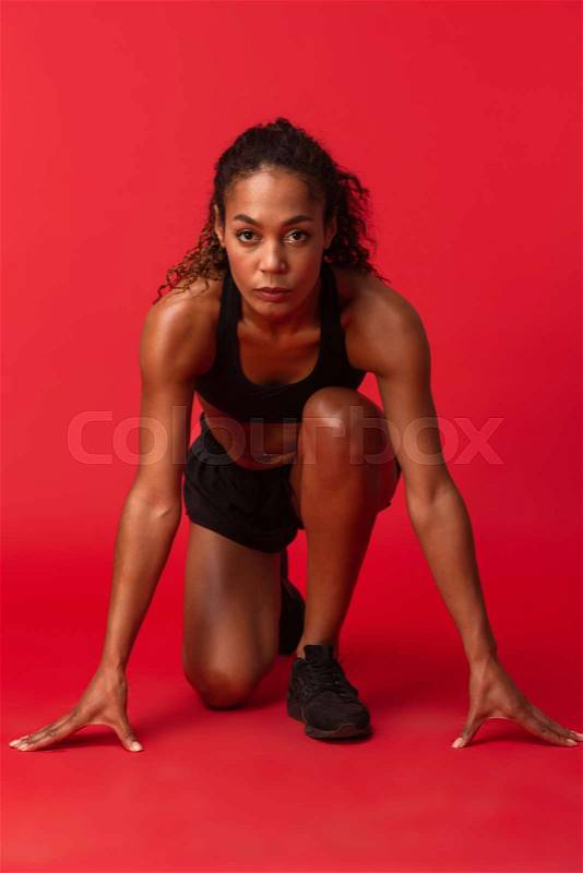 Portrait of strong african american woman in black sportswear running, isolated over red background, stock photo