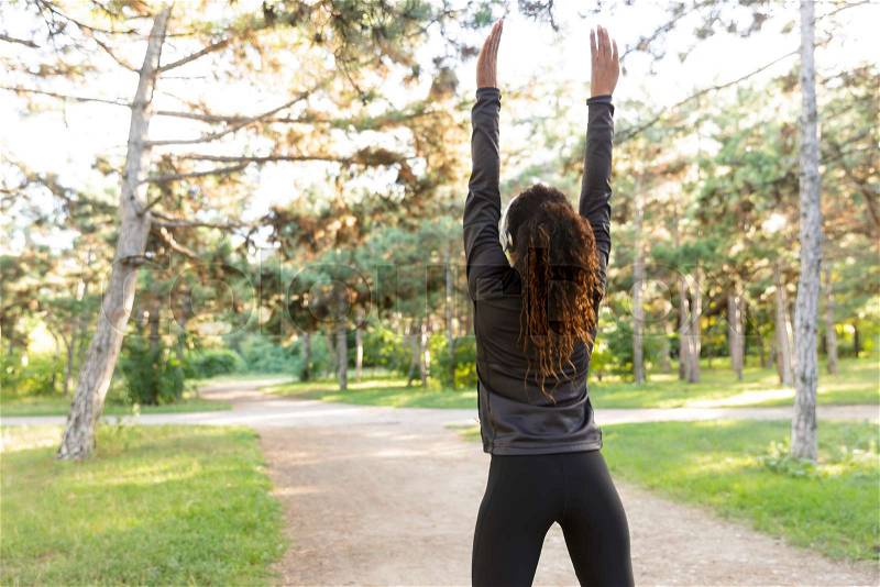 Image of skinny woman 20s wearing black tracksuit working out, and stretching body in green park, stock photo