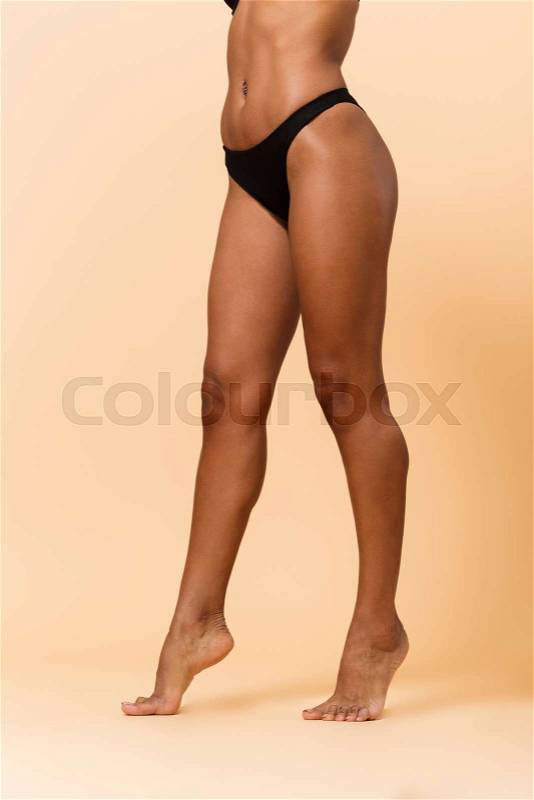 Cropped portrait of skinny woman 20s wearing black lingerie, standing isolated over beige background, stock photo