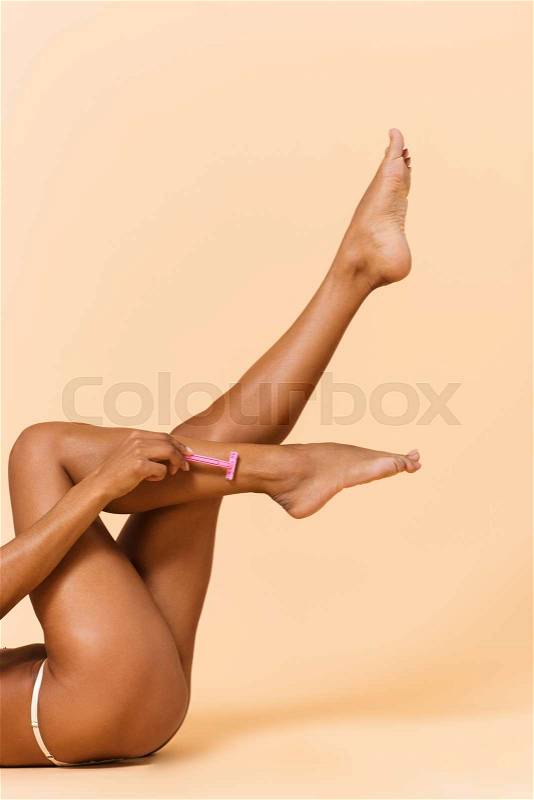 Cropped portrait of sexual woman 20s laying on floor with naked legs, isolated over beige background, stock photo