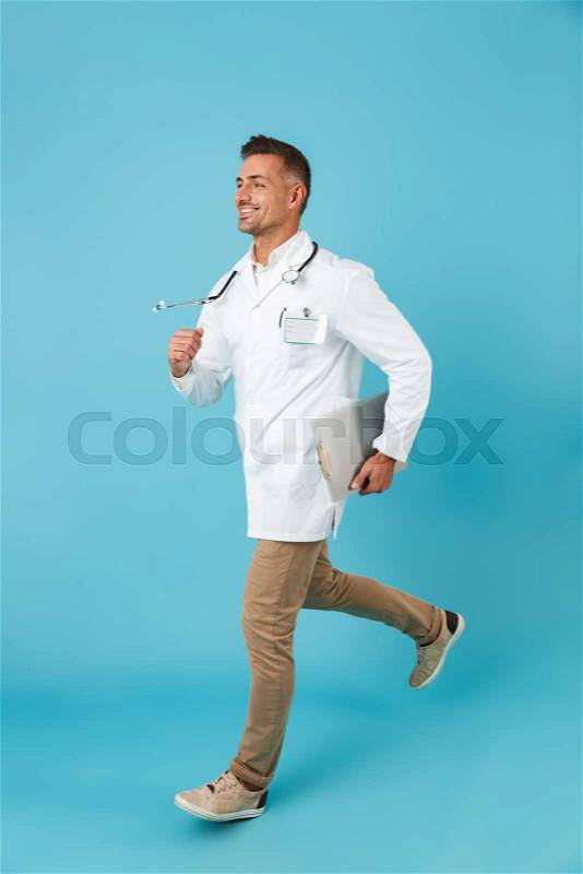 Full length image of joyous man wearing white medical coat and stethoscope running, while isolated over blue background, stock photo