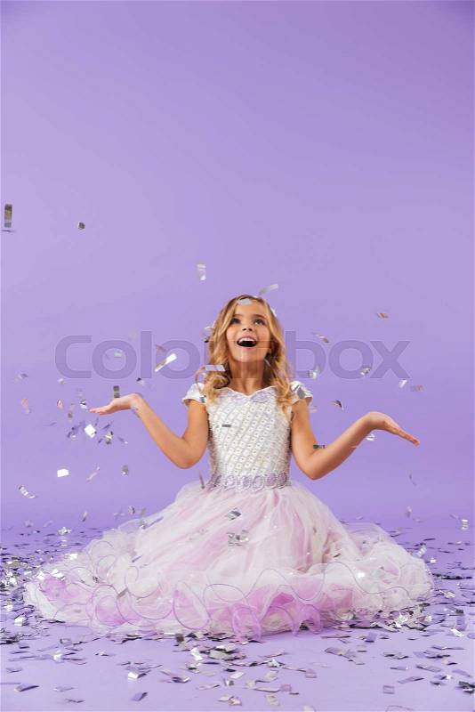 Pretty little girl dressed in princess dress sitting isolated over violet background, stock photo