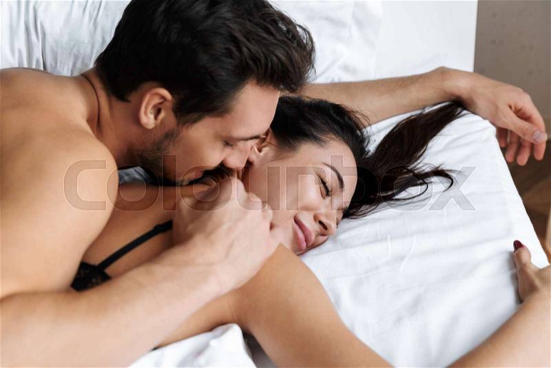 Photo of half-naked couple man and woman hugging together, while lying in bed at home or hotel apartment, stock photo