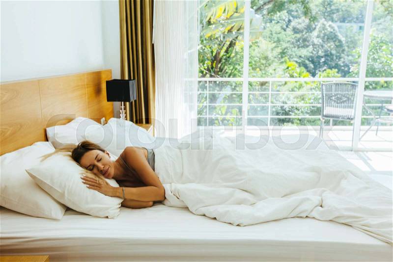 Woman sleeping on bed in luxury hotel room in the morning infront of big window. Chilling well on comfy matress and pillows, stock photo