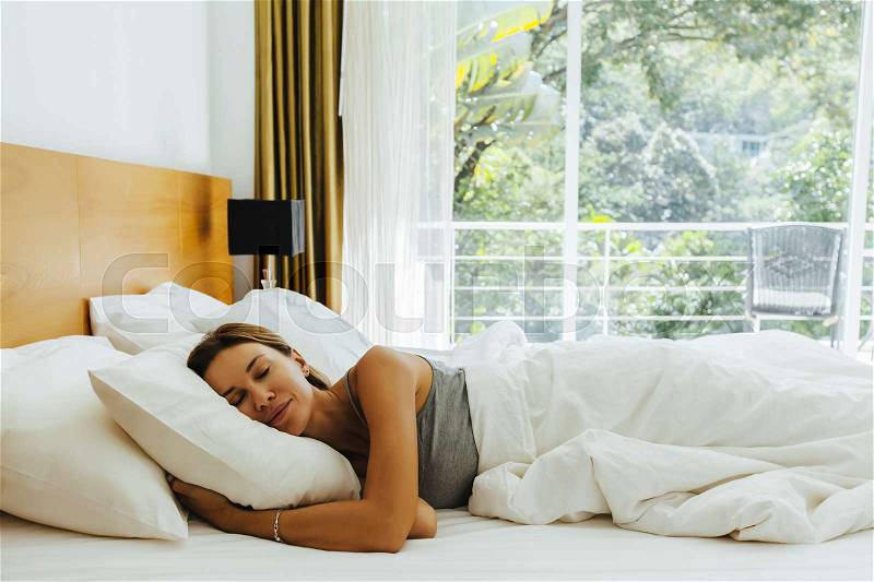 Woman sleeping on bed in luxury hotel room in the morning infront of big window. Chilling well on comfy matress and pillows, stock photo